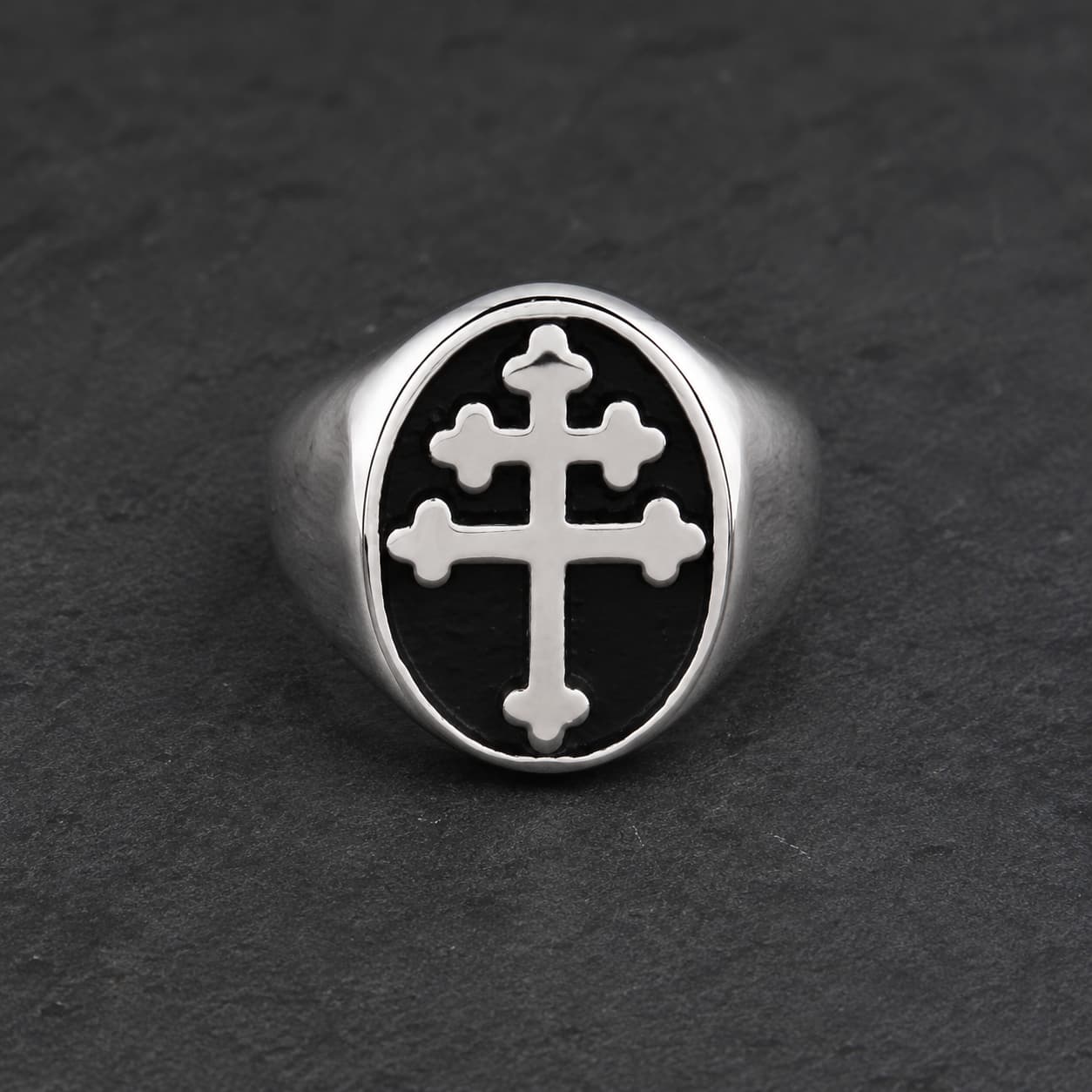 Bague Croix de Lorraine en acier inoxydable argenté avec croix blanche sur fond noir, posée sur pierre sombre