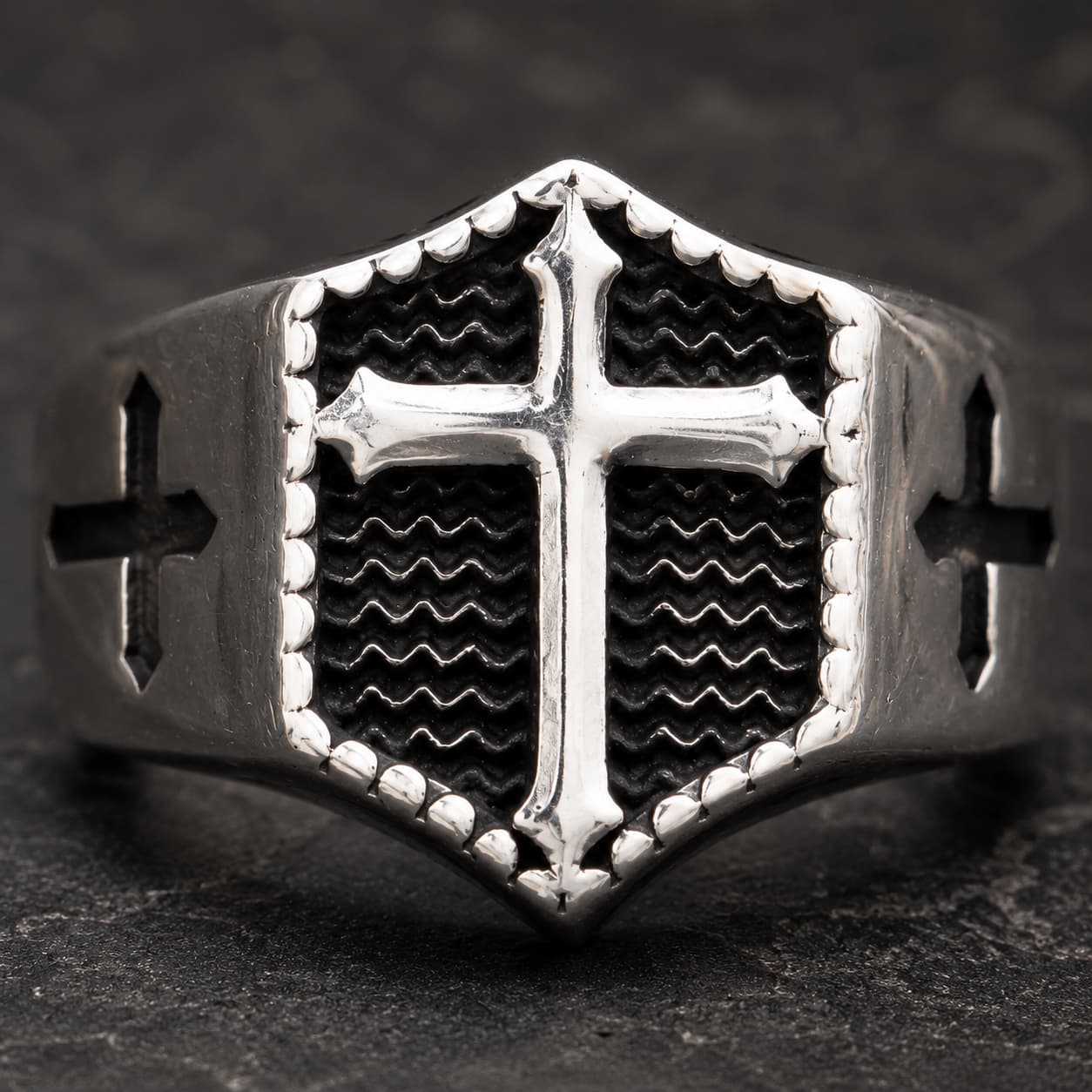 Gros plan de la Bague Croix Impériale en acier inoxydable avec croix blanche en relief sur fond noir ondulé
