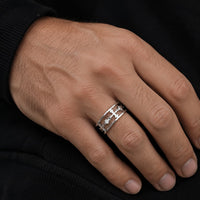 Bague de la Dame du Temple en acier inoxydable premium portée sur la main d’un homme, avec motif croix ajourée argentée visible en gros plan sur fond sombre.