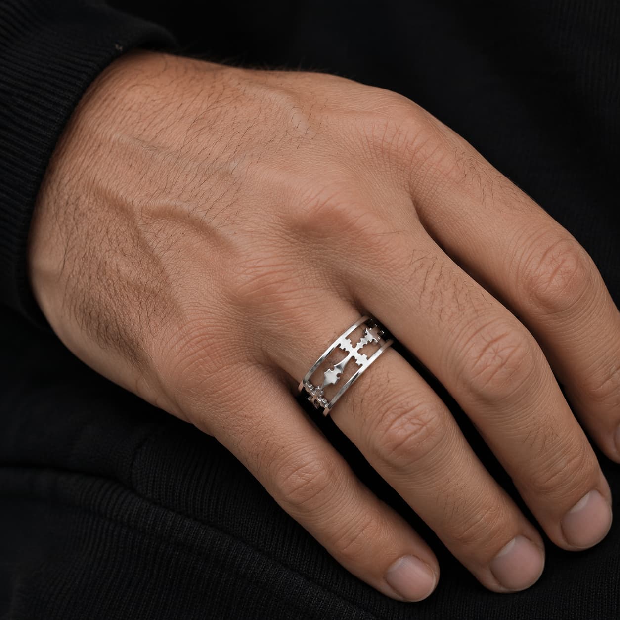 Bague de la Dame du Temple en acier inoxydable premium portée sur la main d’un homme, avec motif croix ajourée argentée visible en gros plan sur fond sombre.