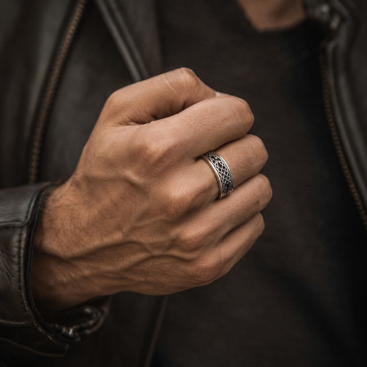 Bague de la Foi Éternelle en acier inoxydable portée à la main par un homme avec veste en cuir noire
