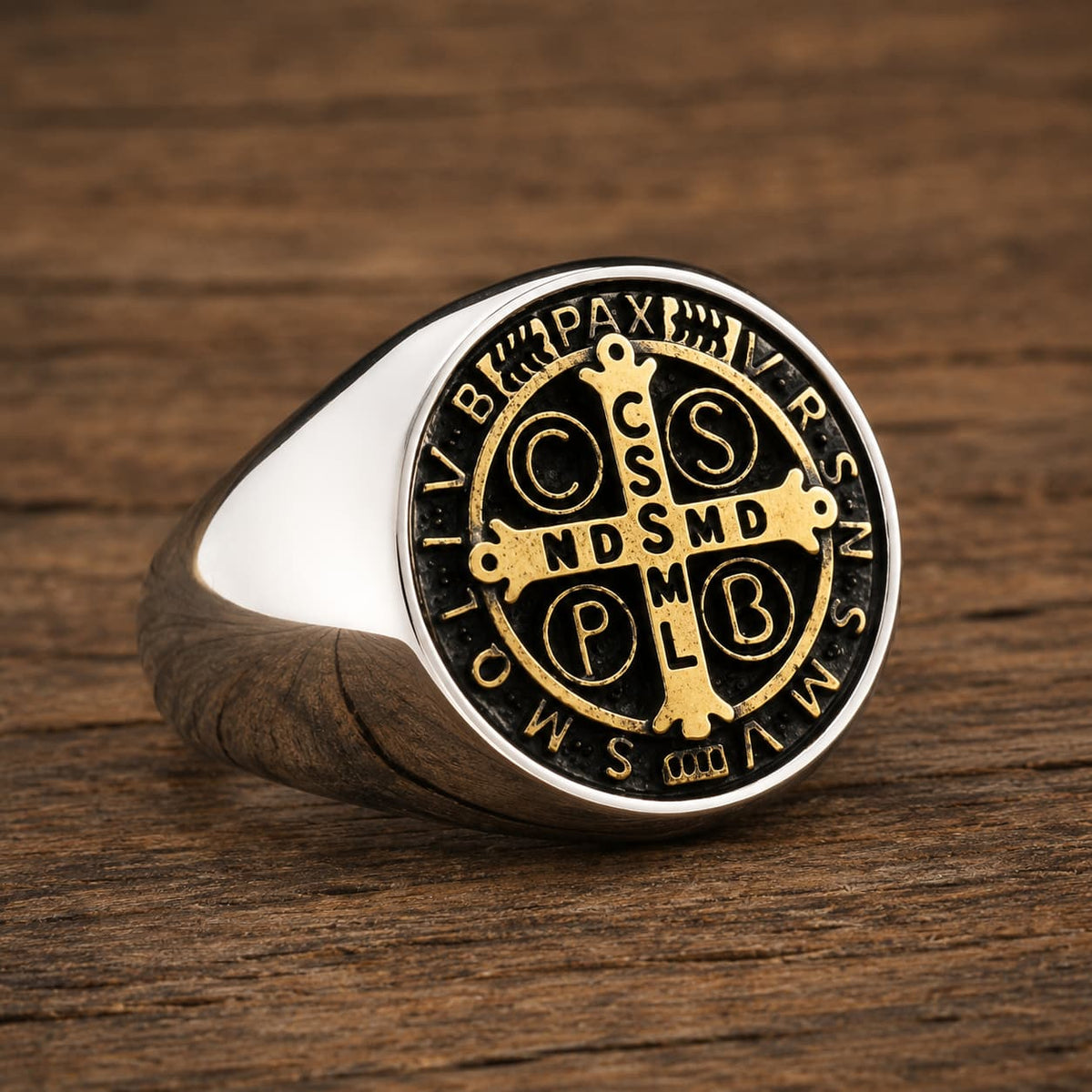 Bague Sacrée des Bénédictins en acier inoxydable avec médaille dorée et noire posée sur bois