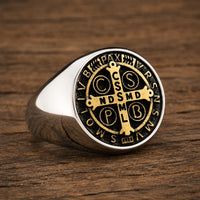 Bague Sacrée des Bénédictins en acier inoxydable avec médaille dorée et noire posée sur bois