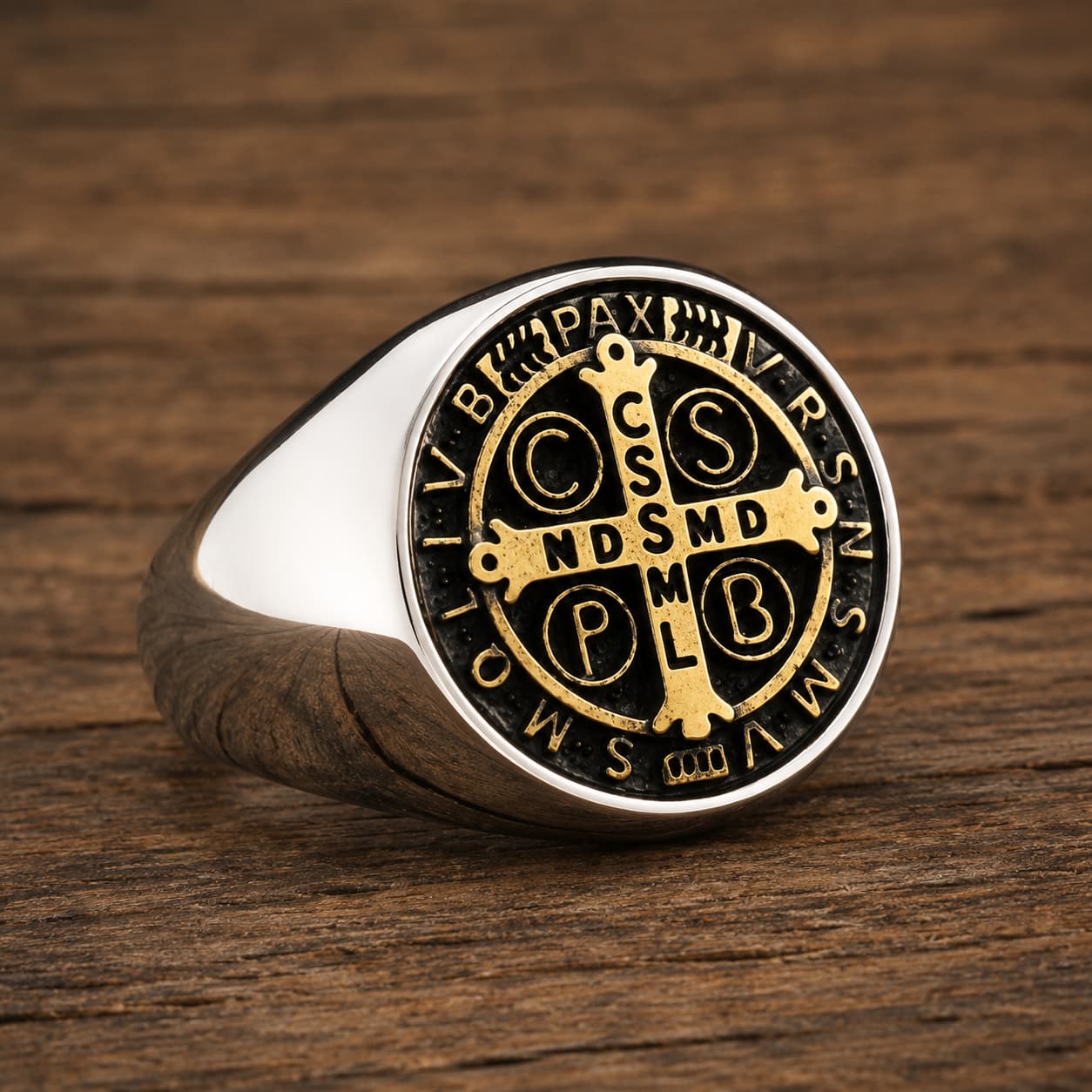 Bague Sacrée des Bénédictins en acier inoxydable avec médaille dorée et noire posée sur bois