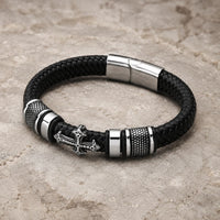 Bracelet de la Basilique en cuir tressé noir et acier inoxydable présenté en vue angle 3/4 sur pierre médiévale claire