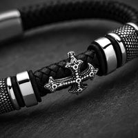 Gros plan du Bracelet de la Basilique avec croix métallique, cuir tressé noir et finitions en acier inoxydable