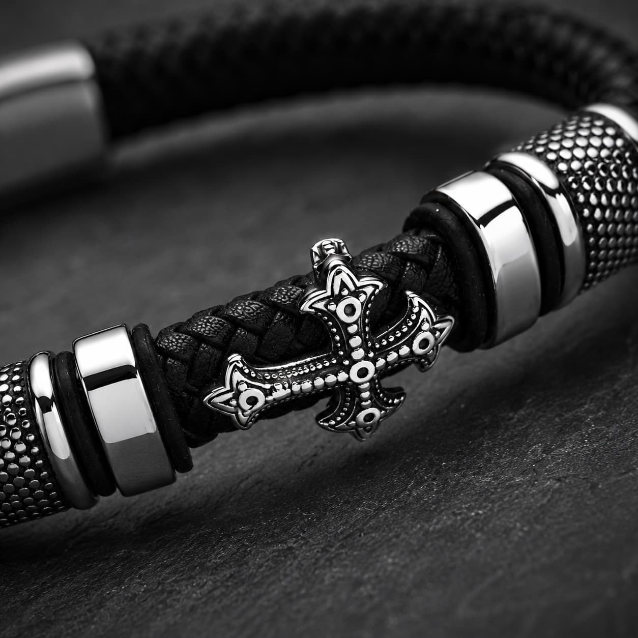 Gros plan du Bracelet de la Basilique avec croix métallique, cuir tressé noir et finitions en acier inoxydable