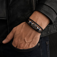 Bracelet de la Commanderie en cuir véritable porté au poignet par un homme avec tenue sombre