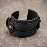 Bracelet de la Vaillance du Croisé en cuir véritable noir renforcé présenté en vue angle 3/4 sur pierre médiévale claire