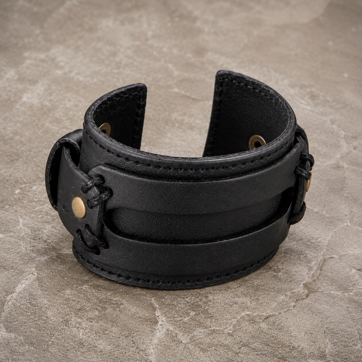 Bracelet de la Vaillance du Croisé en cuir véritable noir renforcé présenté en vue angle 3/4 sur pierre médiévale claire