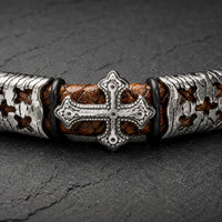 Gros plan de la croix du Bracelet de l’Indulgence en cuir tressé marron et acier inoxydable