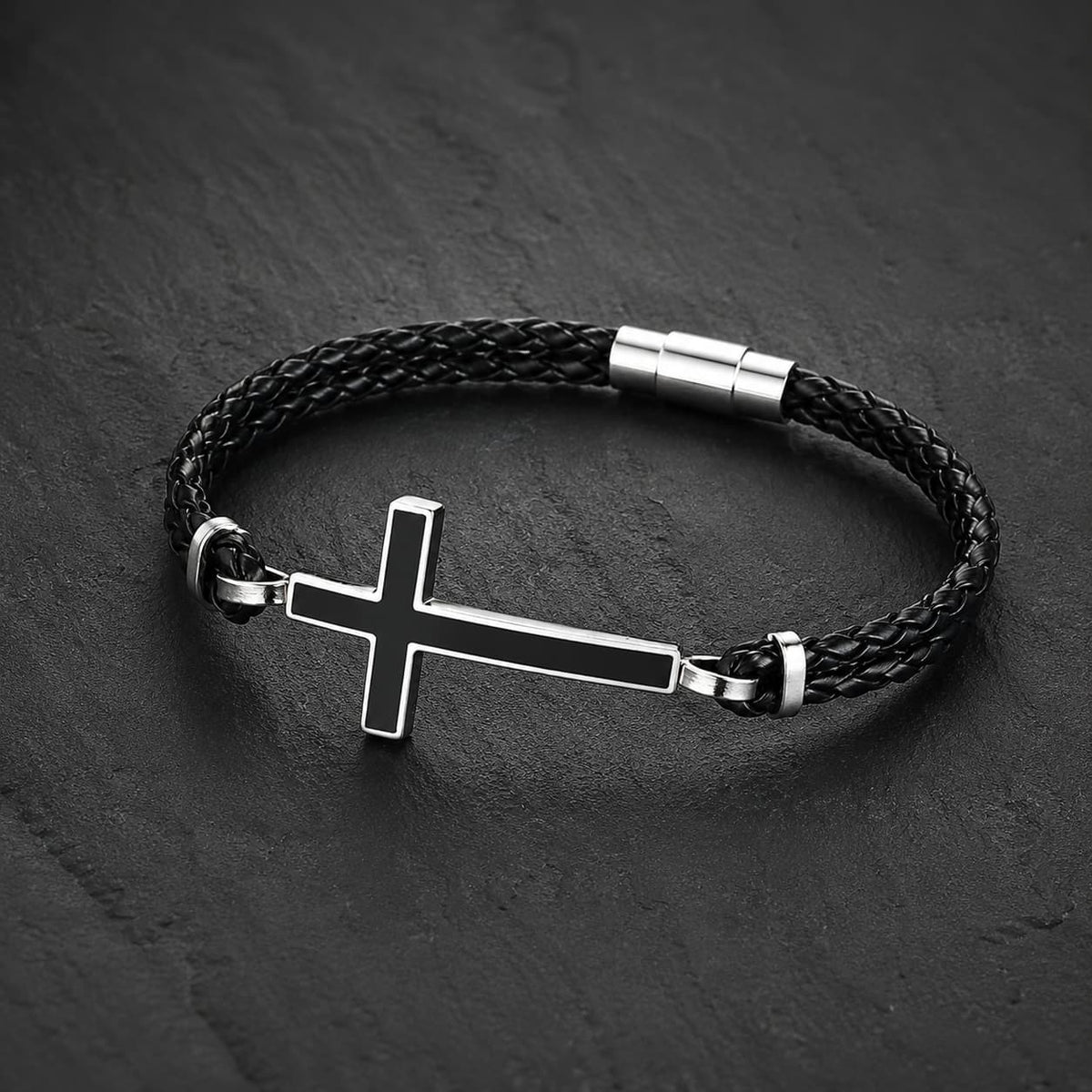 Bracelet de la Loyauté Sacrée en cuir tressé noir avec croix en acier inoxydable présenté sur ardoise sombre