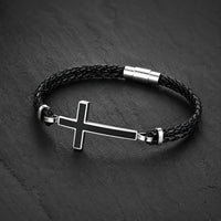 Bracelet de la Loyauté Sacrée en cuir tressé noir avec croix en acier inoxydable présenté sur ardoise sombre