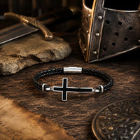 Bracelet de la Loyauté Sacrée en cuir tressé noir dans un décor médiéval avec casque, épée, bois ancien et parchemin