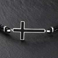 Gros plan du Bracelet de la Loyauté Sacrée avec croix noire bordée d’acier inoxydable et cuir tressé noir