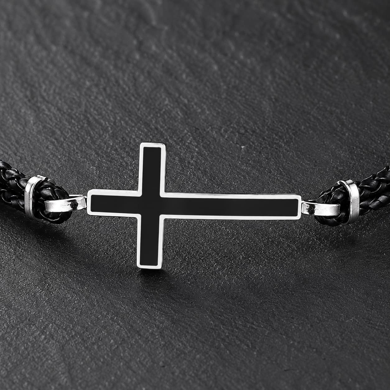 Gros plan du Bracelet de la Loyauté Sacrée avec croix noire bordée d’acier inoxydable et cuir tressé noir