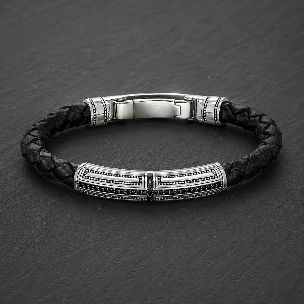 Bracelet du Primat Sacré en argent 925 sterling avec cuir tressé noir présenté en vue angle 3/4 sur ardoise sombre