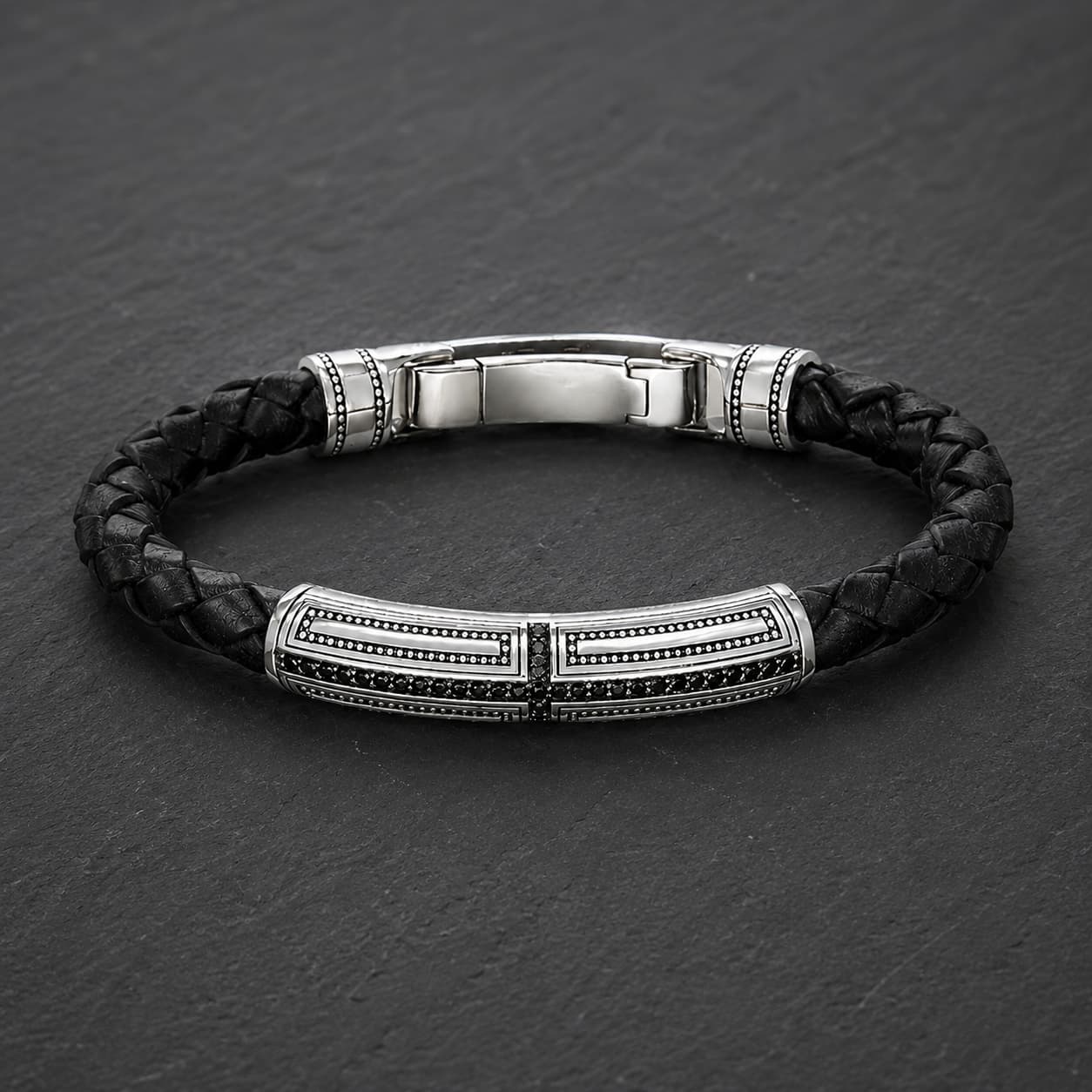 Bracelet du Primat Sacré en argent 925 sterling avec cuir tressé noir présenté en vue angle 3/4 sur ardoise sombre