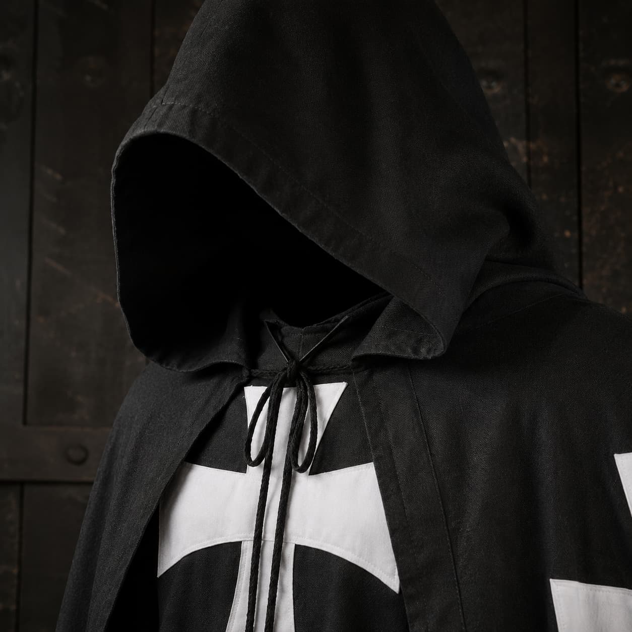 Gros plan de la Cape de la Confrérie Templière en nylon noir avec capuche, cordon et croix blanche.