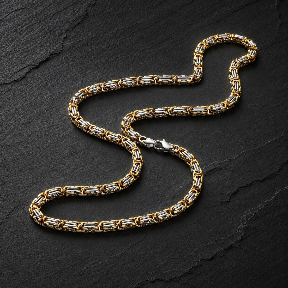 Chaîne du Temple en acier inoxydable premium, finition bicolore dorée et argentée, présentée sur fond anthracite texturé.
