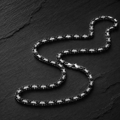 Chaîne du Temple en acier inoxydable premium noire et argentée sur fond anthracite texturé.
