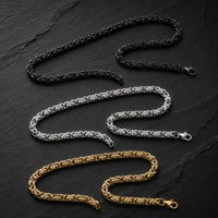 Variantes noir, argent et doré de la Chaîne du Temple en acier inoxydable premium présentées sur fond sombre.
