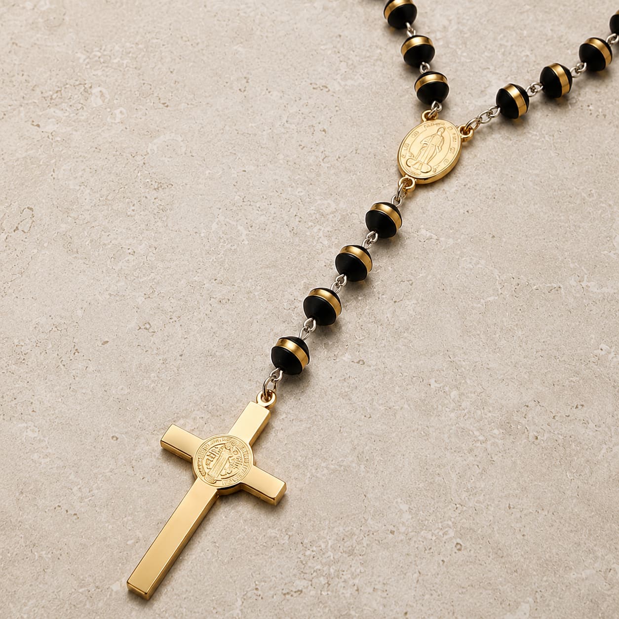 Gros plan sur la croix et les perles du Chapelet de l’Ordre Sacré en acier inoxydable sur fond pierre beige-gris.