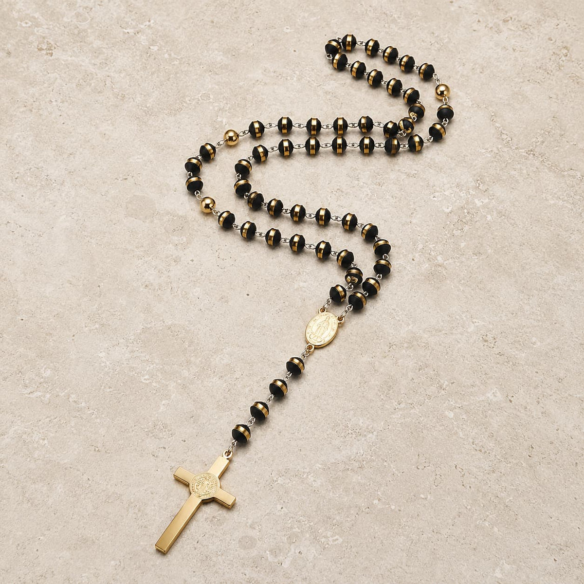 Chapelet de l’Ordre Sacré en acier inoxydable avec perles noires et dorées sur fond pierre médiévale claire.