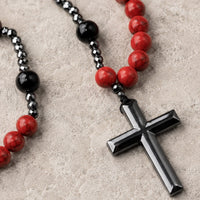 Gros plan de la croix noire du Chapelet de la Sacristie avec perles rouges et noires sur pierre médiévale claire.