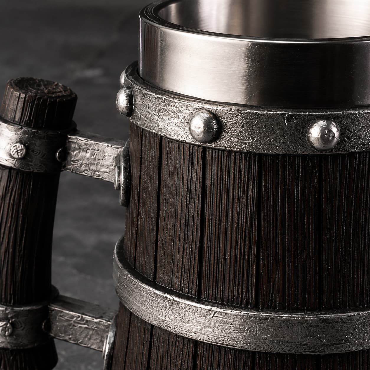 Gros plan sur la texture bois sombre et les cerclages en métal riveté de la Chope de Bière du Temple.