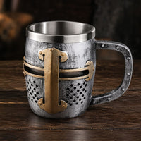 Chope du Heaume Templier en résine et acier inoxydable présentée en vue angle sur une table en bois ancien sombre.