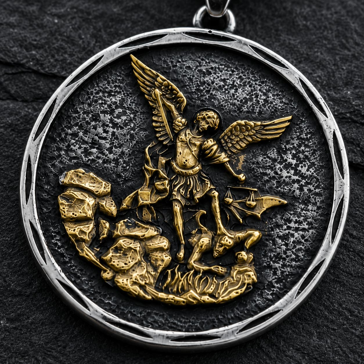 Gros plan du pendentif Bouclier de Saint Michel en acier inoxydable sur fond anthracite texturé ardoise sombre.