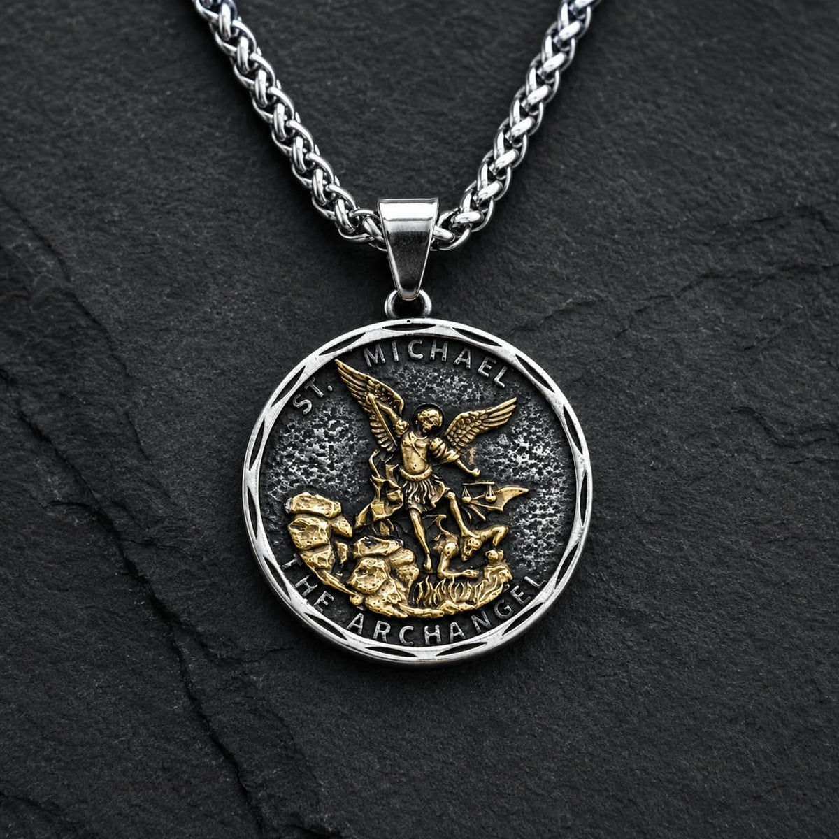 Collier Bouclier de Saint Michel en acier inoxydable avec médaille argentée et dorée sur fond anthracite texturé.
