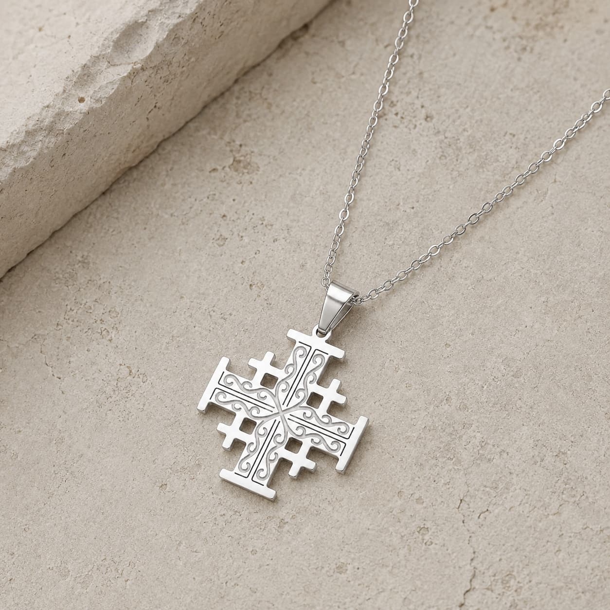 Vue angle 3/4 du Collier Croix de l'Ordre de Jérusalem en acier inoxydable premium sur pierre médiévale claire.