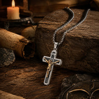 Collier Croix de la Passion en acier inoxydable argenté avec Christ doré dans une ambiance médiévale avec bois ancien et lumière chaude.