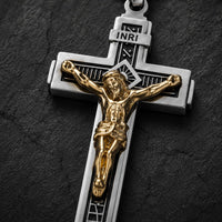 Gros plan du pendentif Croix de la Passion en acier inoxydable argenté avec Christ doré sur fond anthracite texturé.
