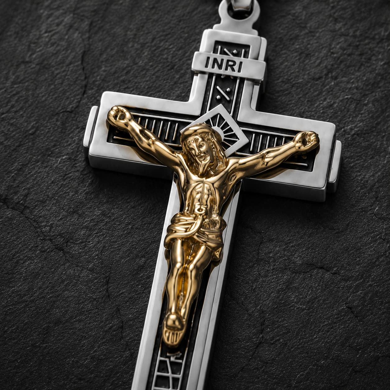 Gros plan du pendentif Croix de la Passion en acier inoxydable argenté avec Christ doré sur fond anthracite texturé.