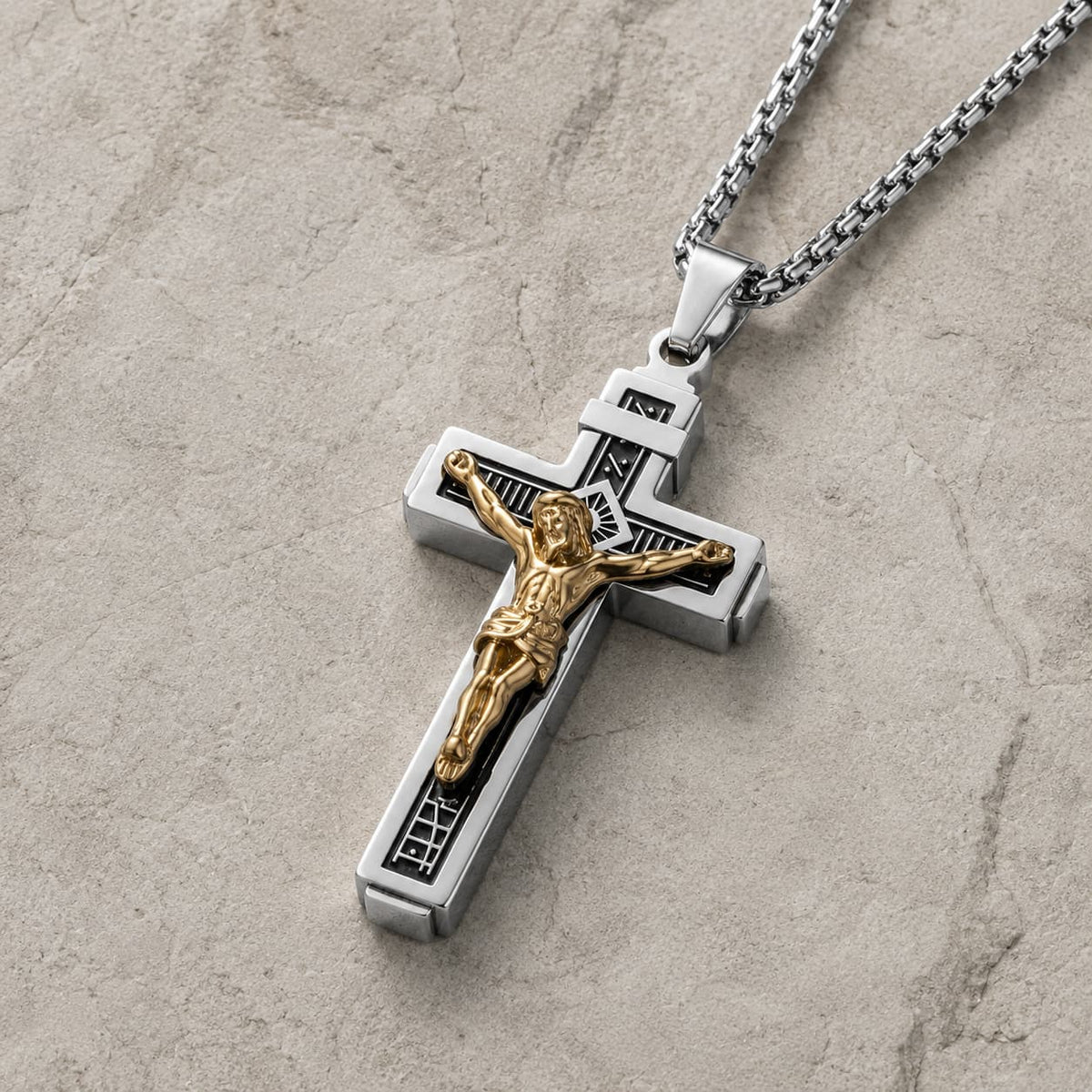 Vue 3/4 du Collier Croix de la Passion en acier inoxydable argenté avec Christ doré sur fond pierre médiévale claire.