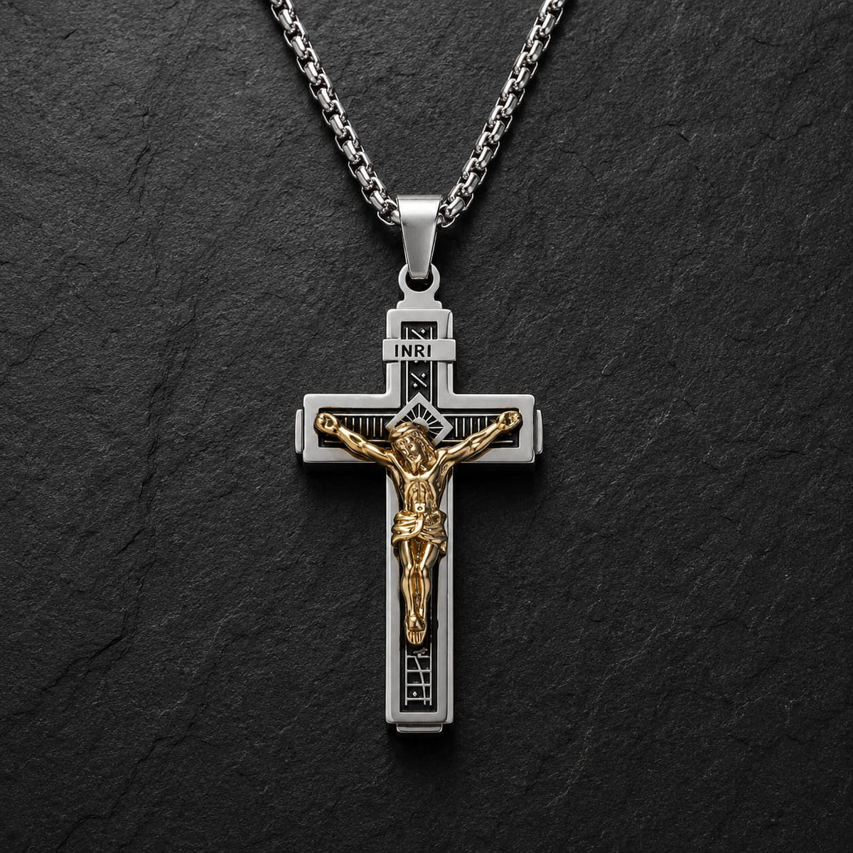 Collier Croix de la Passion en acier inoxydable argenté avec Christ doré sur fond anthracite texturé.