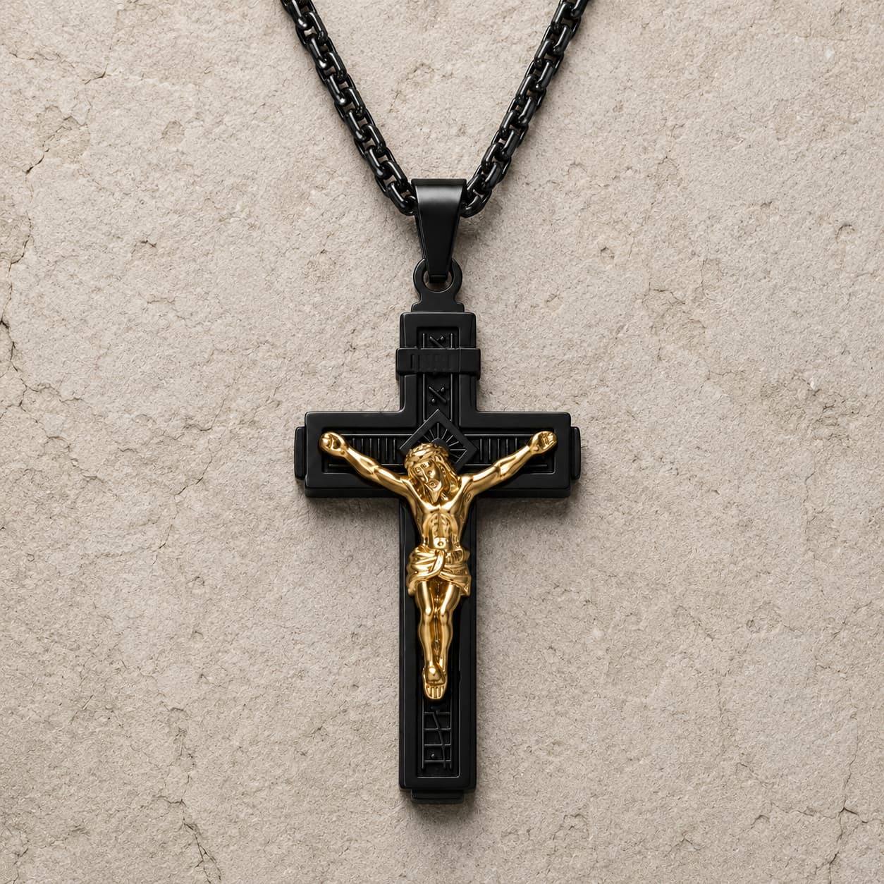 Variante noire du Collier Croix de la Passion en acier inoxydable avec Christ doré sur fond pierre médiévale claire.