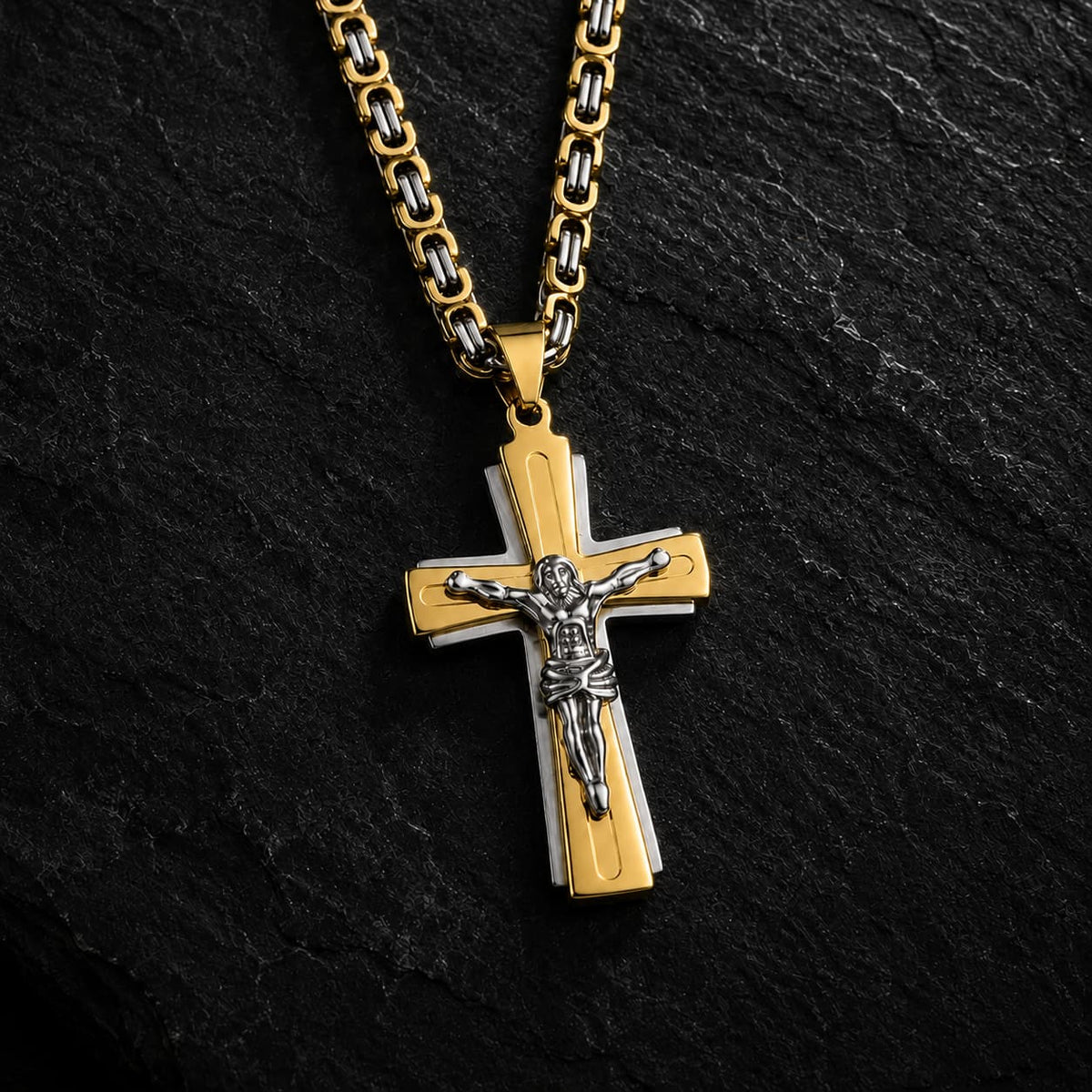 Collier Croix du Christ en acier inoxydable bicolore argenté et doré sur fond anthracite texturé.