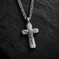 Variante argentée du Collier Croix du Christ en acier inoxydable sur fond anthracite texturé.