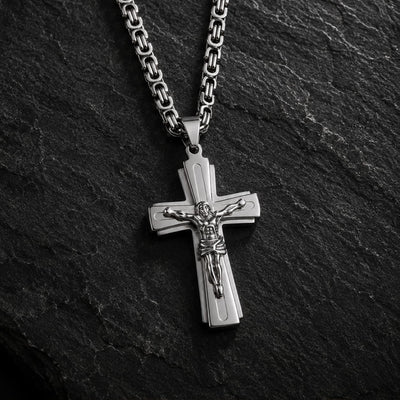 Variante argentée du Collier Croix du Christ en acier inoxydable sur fond anthracite texturé.