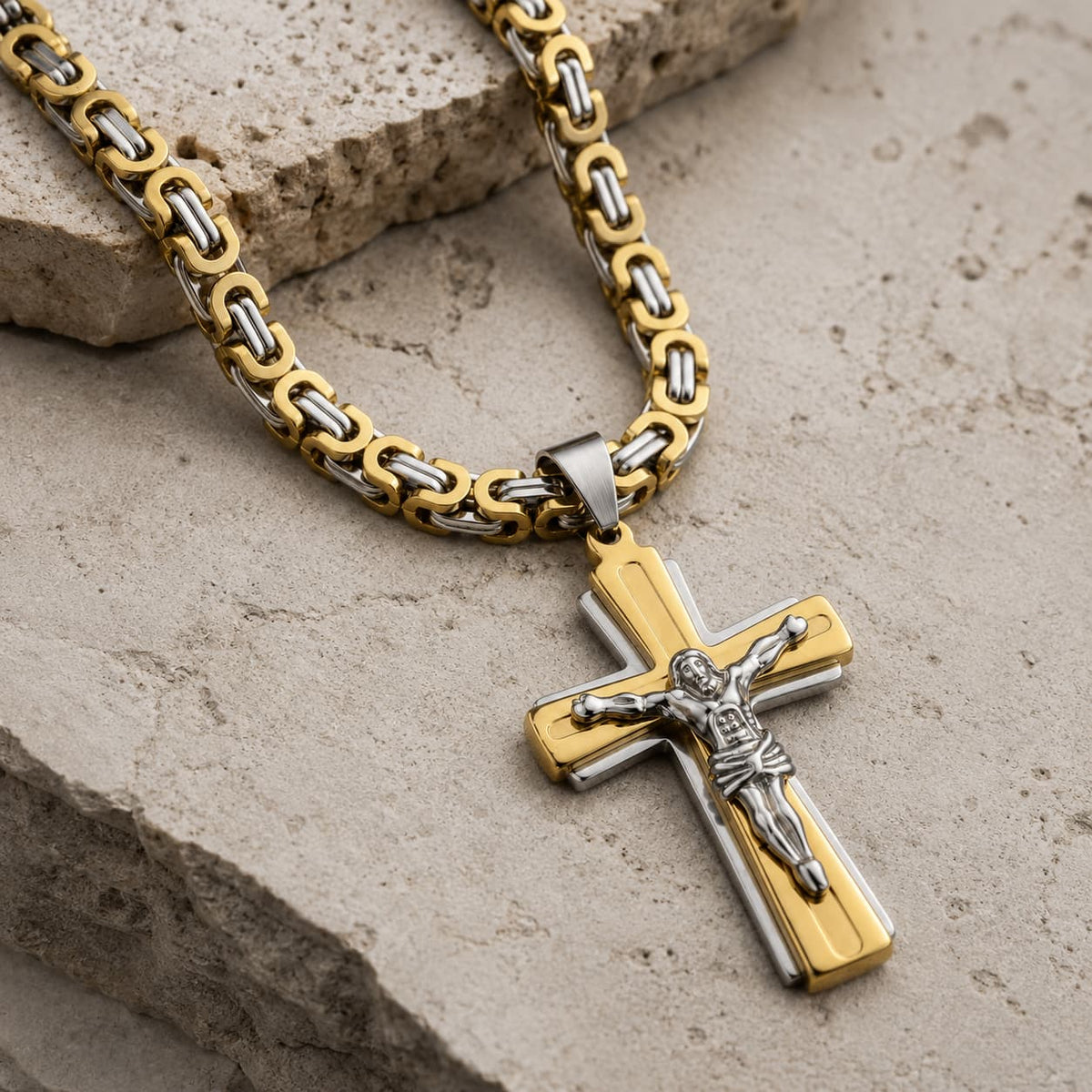 Vue angle 3/4 du Collier Croix du Christ en acier inoxydable argenté et doré sur pierre médiévale claire.
