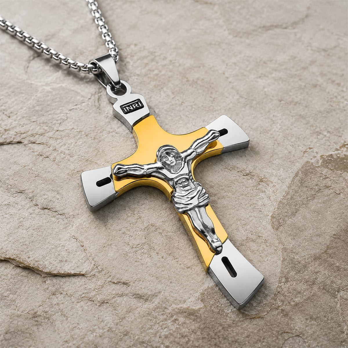 Collier de l’Ascension du Croisé en acier inoxydable doré et argenté avec pendentif crucifix en vue angle 3/4 sur pierre médiévale claire
