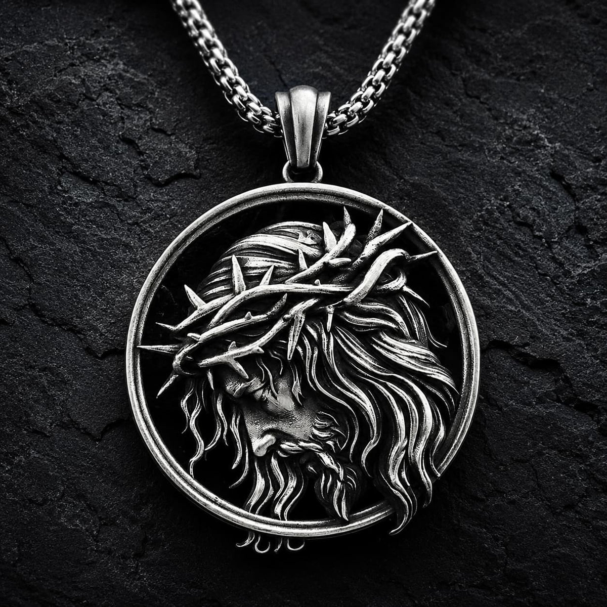 Collier de l’Espoir du Christ en acier inoxydable avec médaillon du Christ couronné d’épines sur fond anthracite texturé.