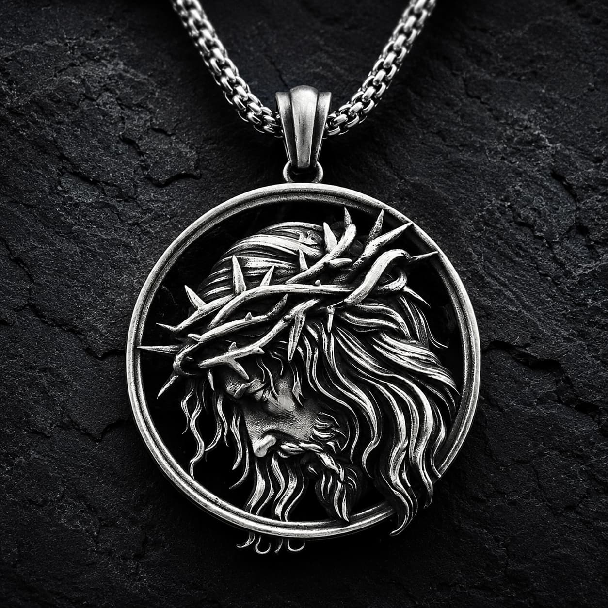 Collier de l’Espoir du Christ en acier inoxydable avec médaillon du Christ couronné d’épines sur fond anthracite texturé.