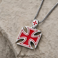 Collier de la Bravoure Templière en acier inoxydable avec pendentif croix rouge posé sur pierre médiévale claire