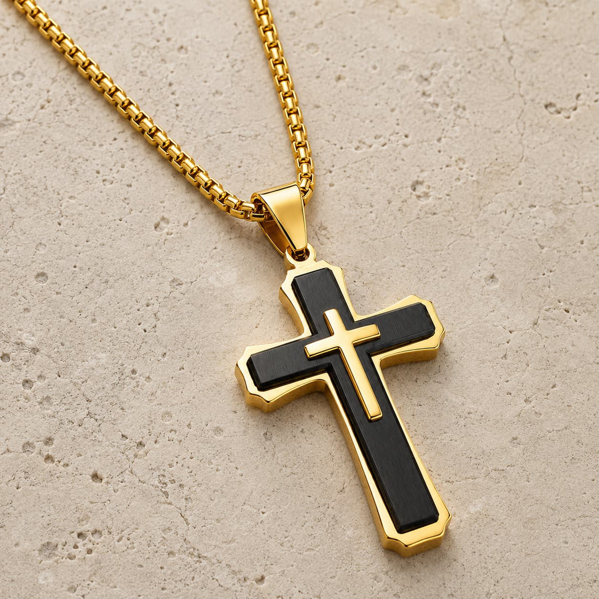 Collier croix noire et dorée en acier inoxydable présenté sur pierre médiévale claire