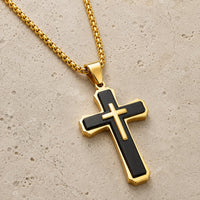 Collier croix noire et dorée en acier inoxydable présenté sur pierre médiévale claire